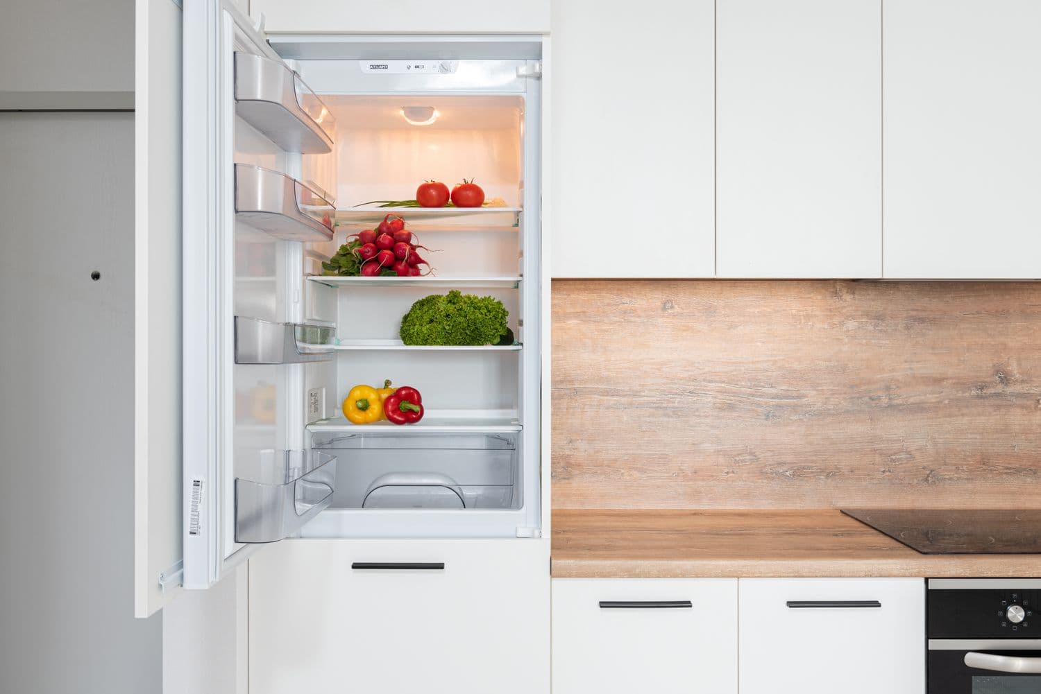An open refrigerator with fresh produce in a white kitchen