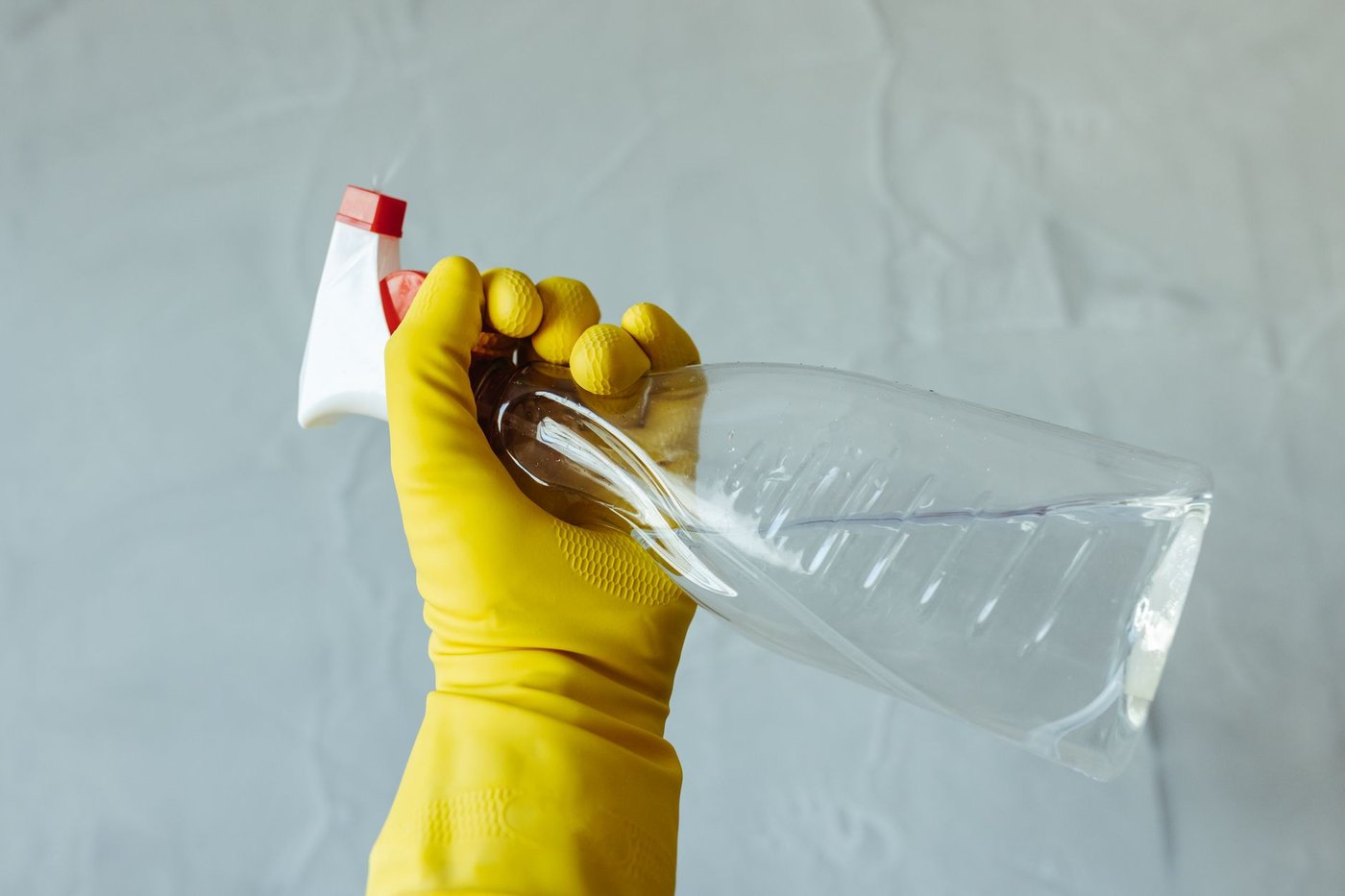 Gloved hand holding a clear spray bottle of cleaner