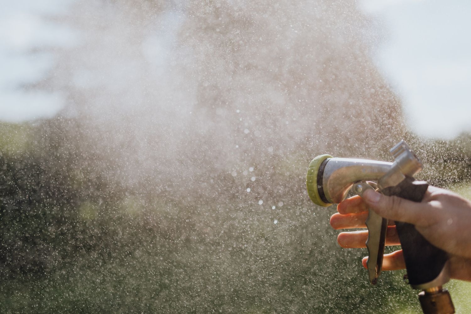 Spraying water outdoors with a garden hose nozzle in low sun