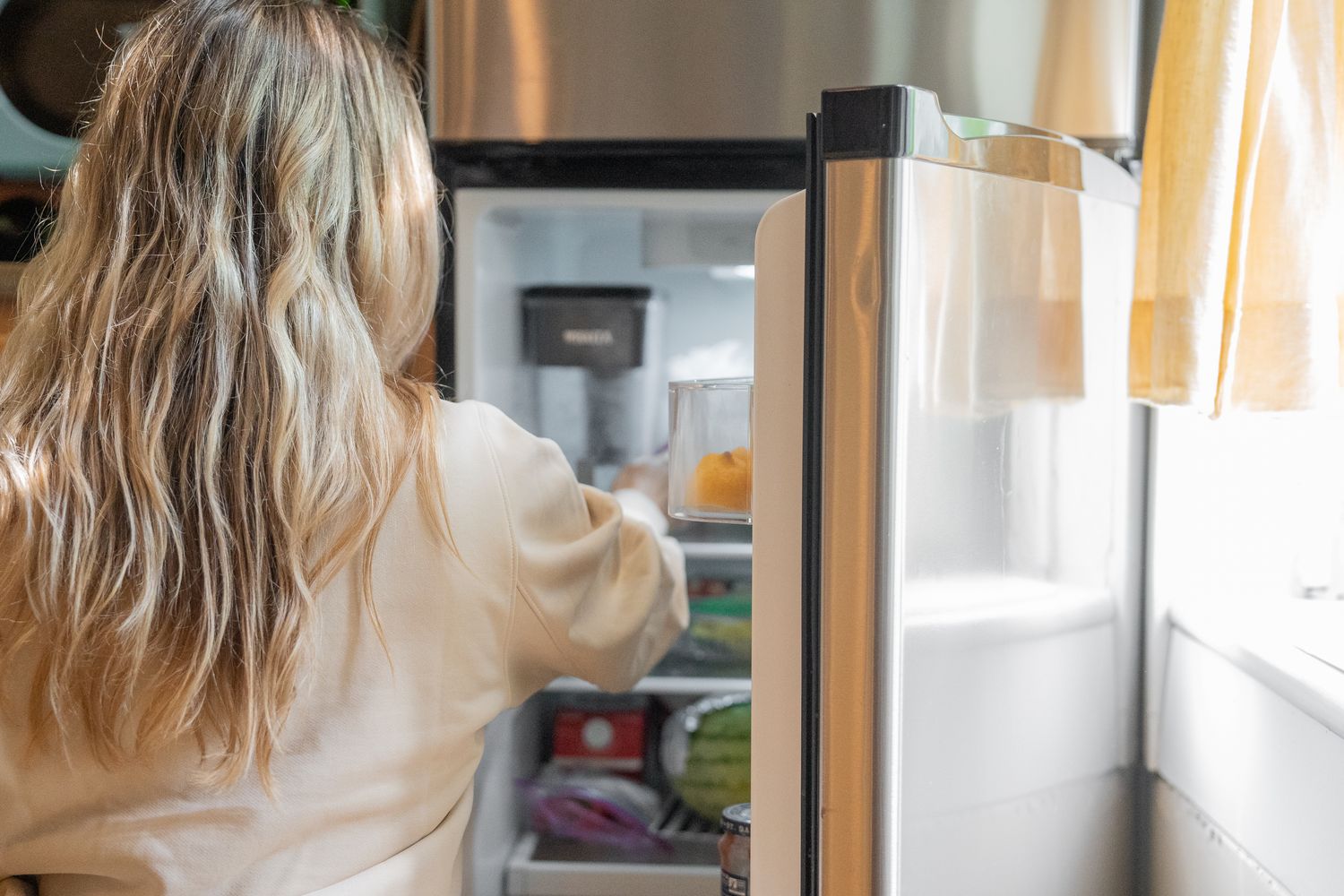 Reaching into an open stainless refrigerator to clear a shelf