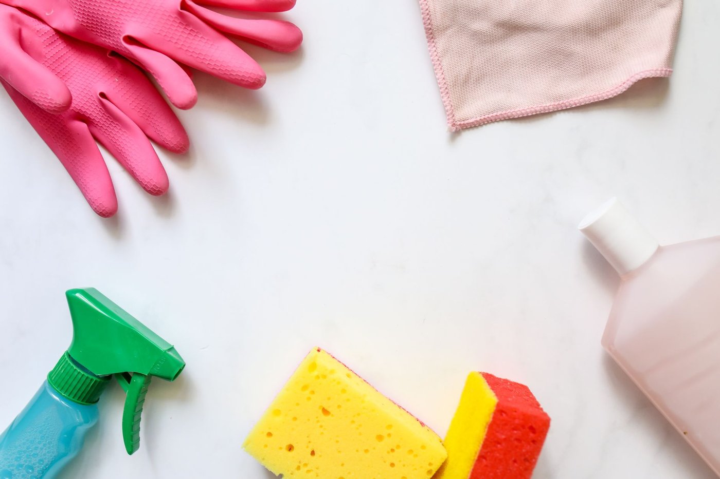 Flat lay of cleaning supplies: gloves, sponges, a spray bottle, and a microfiber cloth