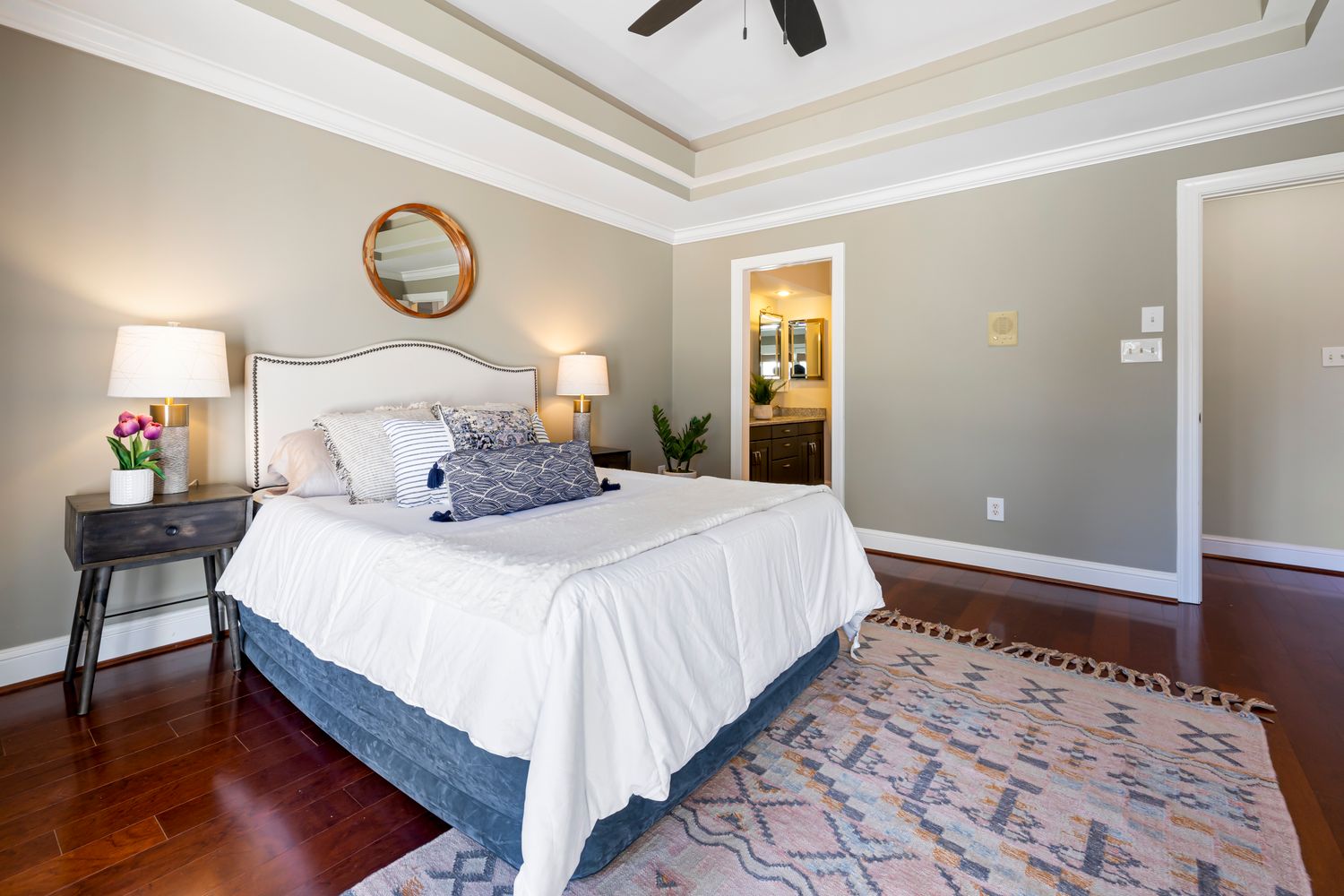 A staged bedroom with a bed skirt meeting a dark hardwood floor