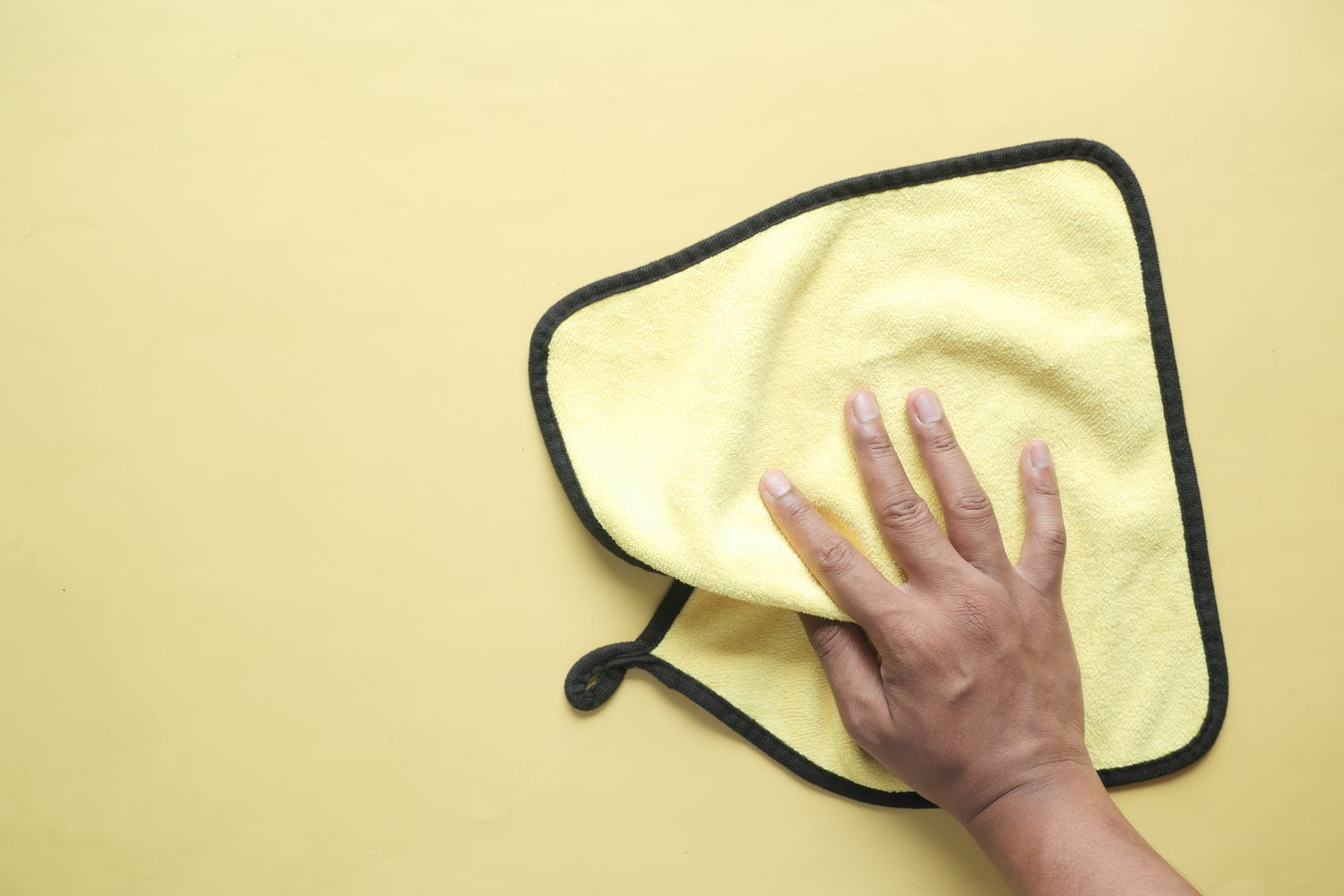 A hand holding a yellow microfiber cloth flat on a surface